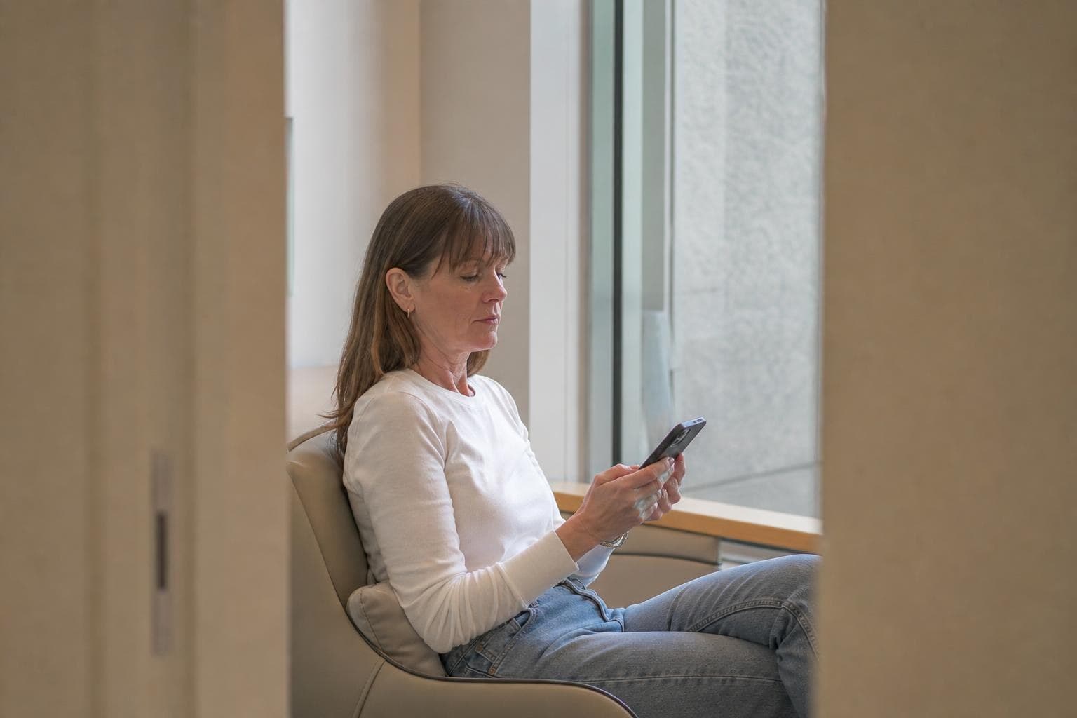 A woman in her forties checking a treatment price list on her phone in a Gangnam clinic waiting area