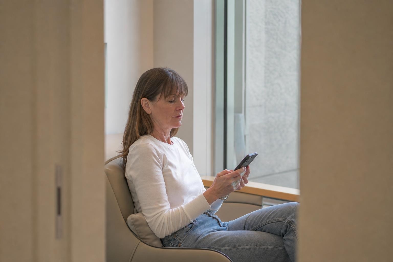 A woman in her forties checking a treatment price list on her phone in a Gangnam clinic waiting area